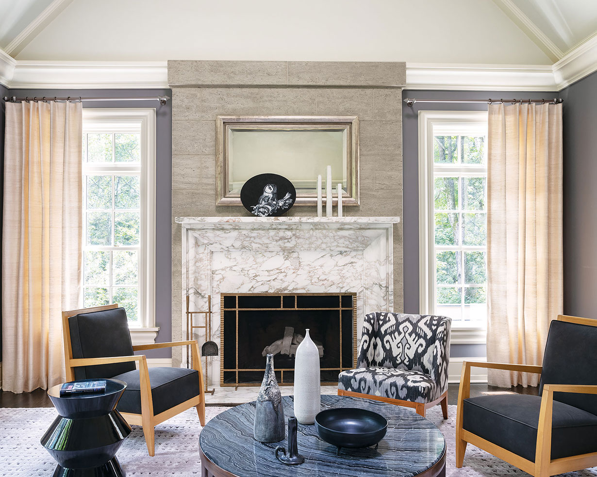 FIREPLACE | A Gascogne Bleu limestone wall frames the classic Calacatta marble fireplace with a custom-designed bronze screen and fire tools. A Shelly Reed oil-on-canvas painting of an owl draws the eye to a silverleaf framed mirror above. Different styling shown in this photo and the one at left demonstrates the room’s versatility.