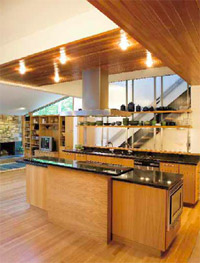 In the kitchen, Atlantic green granite countertops reflect recessed lighting in cedar overhead. The vertical and horizontal orientation of oak cladding is the only ornamentation on the two islands, besides the higher section of countertop that hides the cooktop from the dining area. A suspended range hood continues the open layout of the house. Floating shelves, bracketed invisibly to frameless panels of ribbed glass, cloak another steel-and-oak staircase.